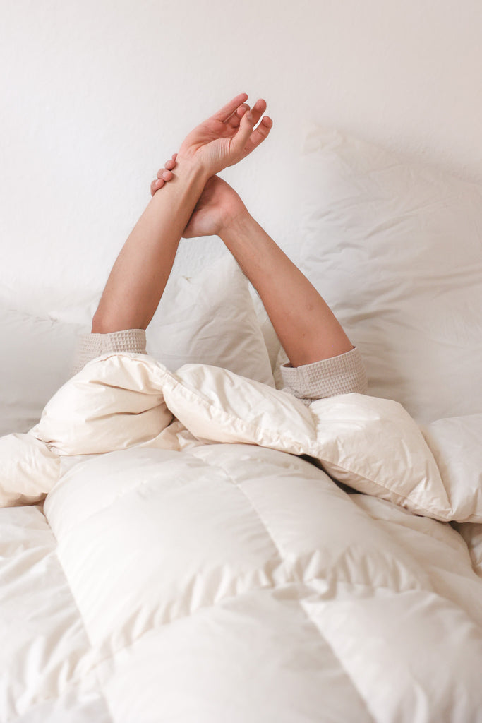 Mensch streckt sich im Bett unter nachhaltiger Daunendecke